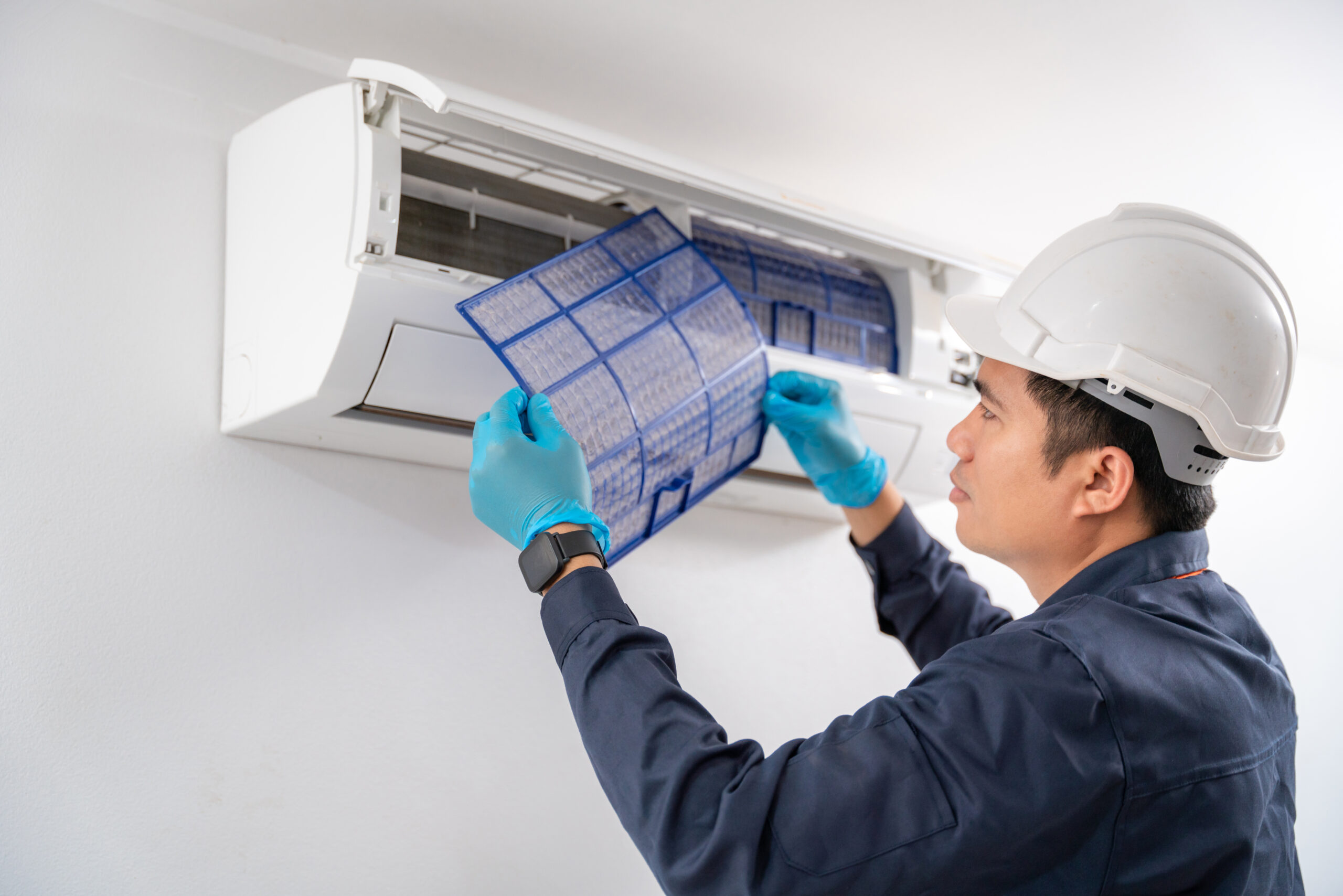 Air conditioner technician removes the air filter to clean the dust of the air conditioner on the white wall.